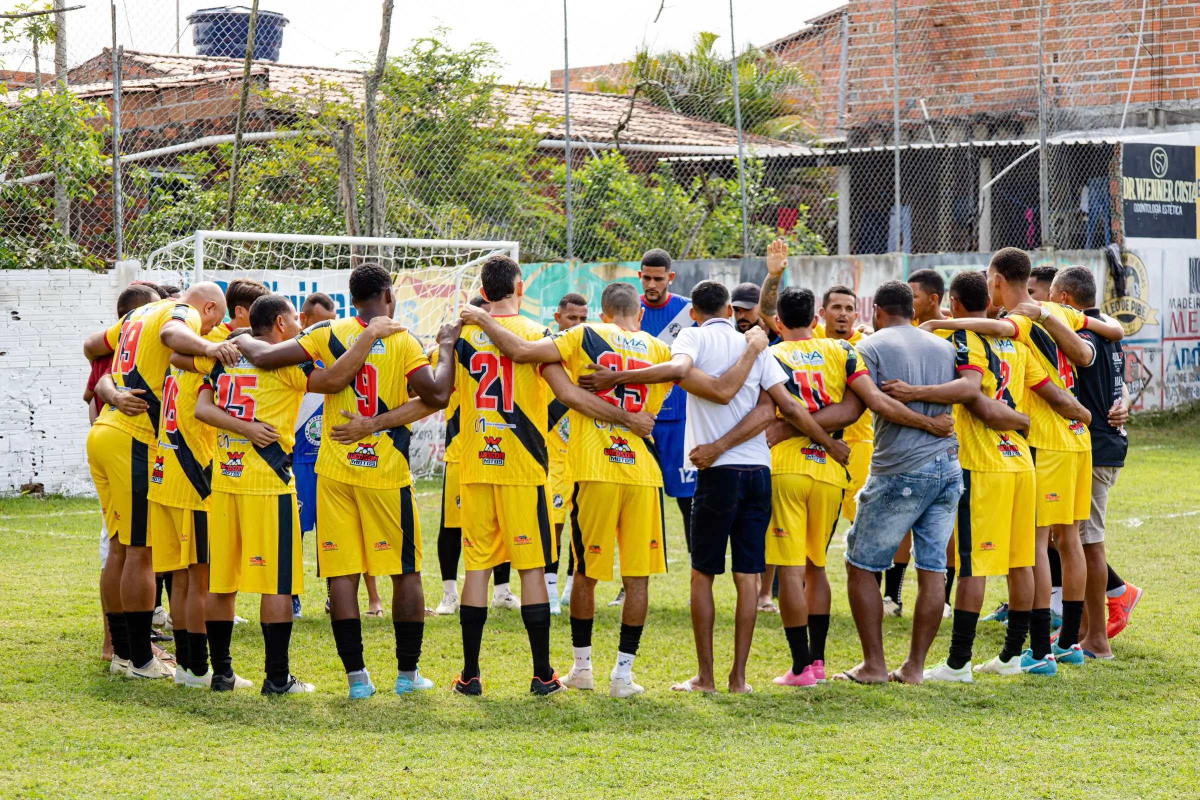 Amateur team in a pre-match huddle, arm in arm, photographed from behind